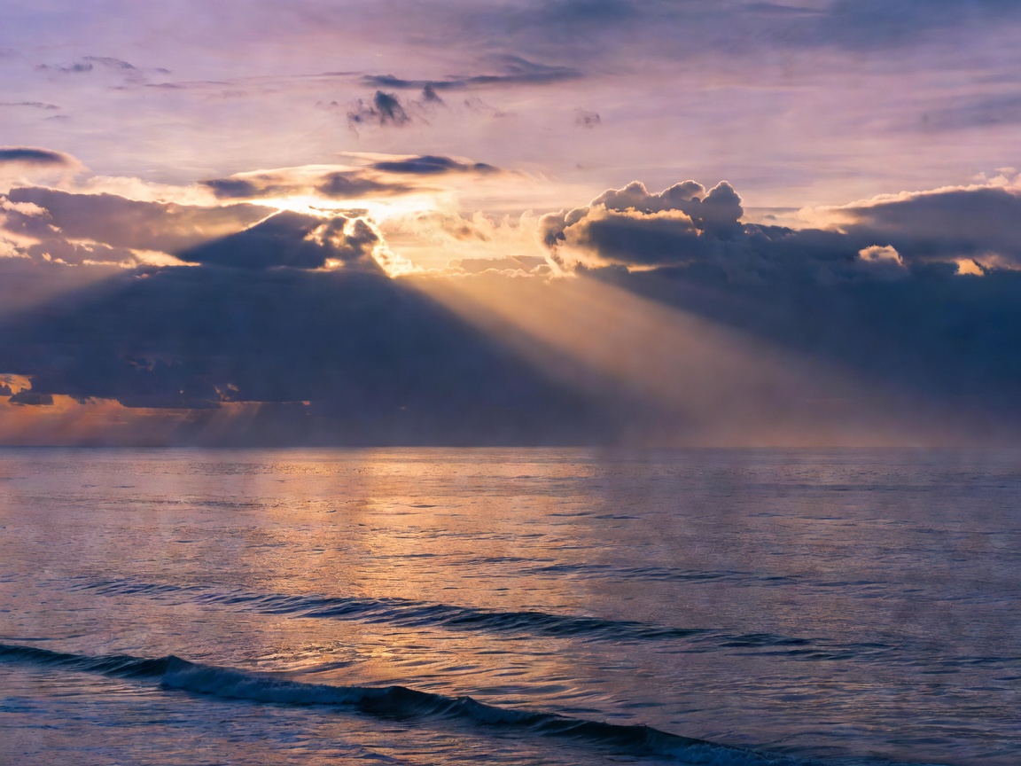 Warm sun rays shining through clouds over sea at twilight